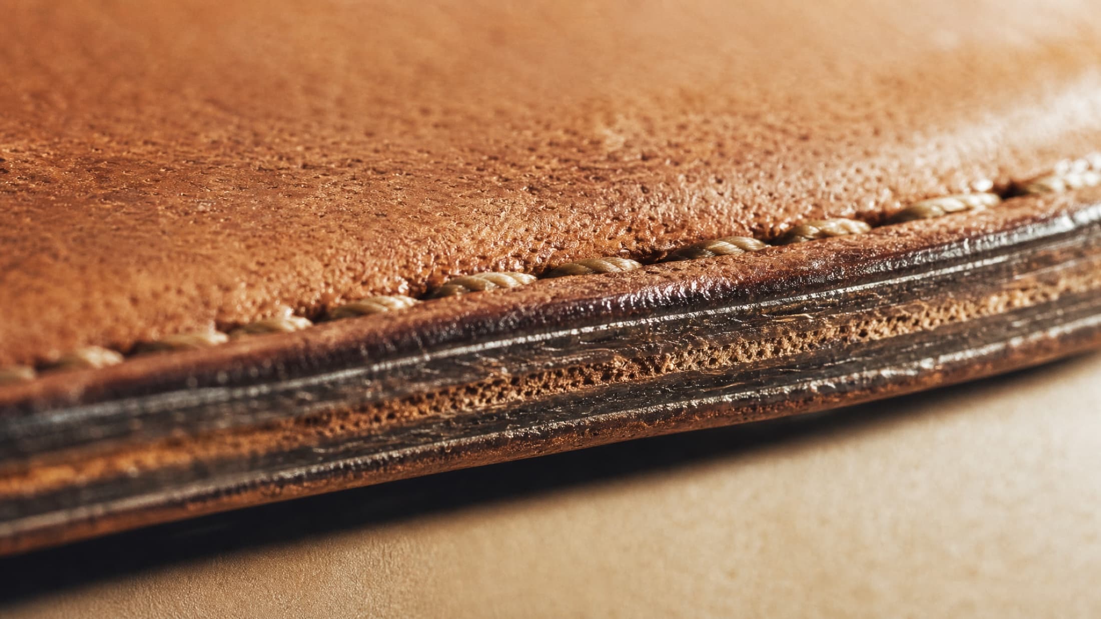 Macro view of a hand-burnished leather edge, the layers of edge paint polished to a glassy finish