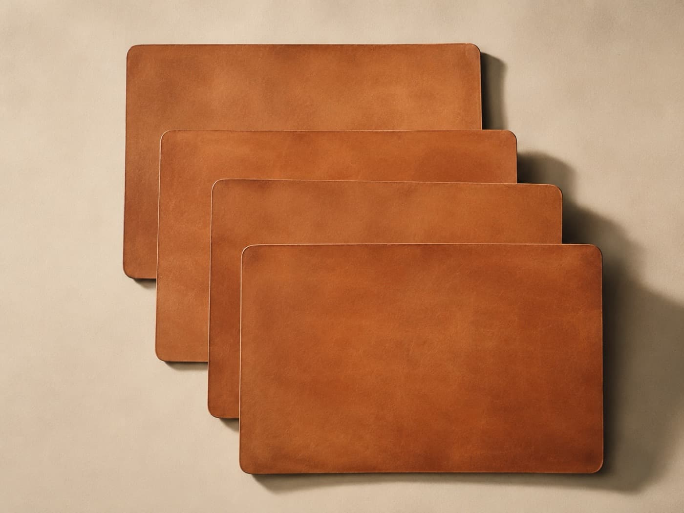 Four large leather placemats stacked with a slight offset, seen from above